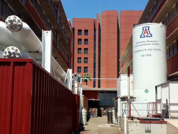 Large cryogenics equipment with red brick UArizona buildings in background