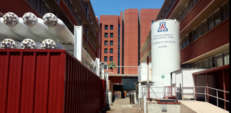 Large cryogenics equipment with red brick UArizona buildings in background
